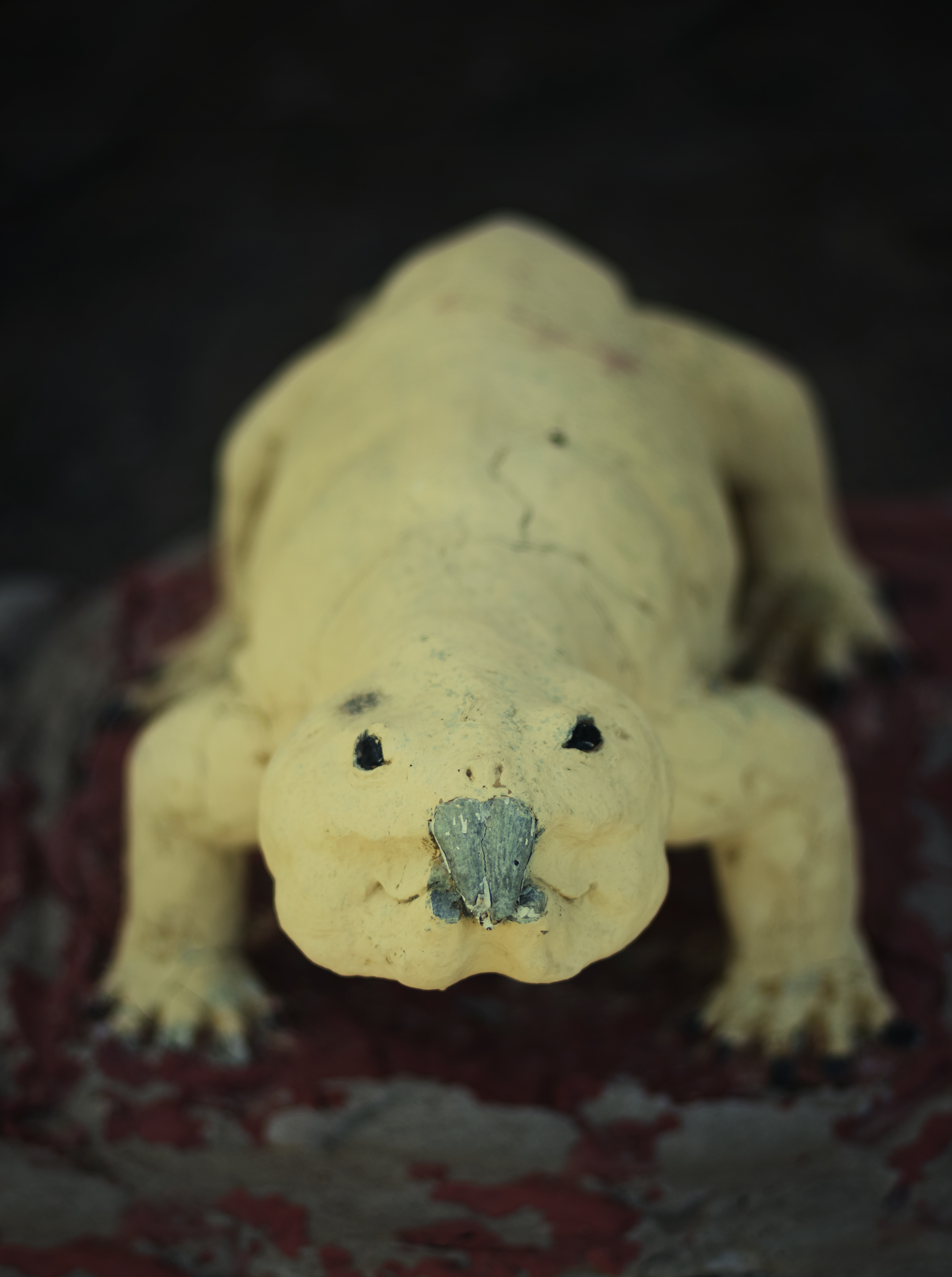 A yellow, lizard-like sculpture with a small grey beak. The up close framing of the sculpture and the shallow depth of field gives it the appearance of a real (yet fantastic) animal.
